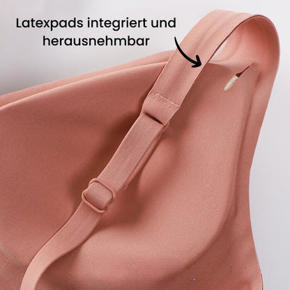 Das Bild zeigt einen Umstandsmode-BH in einem sanften Rosaton, bei dem die Latexpads integriert und herausnehmbar sind. Die Pads bieten zusätzlichen Komfort und können nach Bedarf entfernt werden. Der Text „Latexpads integriert und herausnehmbar“ hebt diese Funktion hervor. Der BH hat verstellbare Träger, die sich leicht anpassen lassen, um eine optimale Passform zu gewährleisten. Die Träger sind mit einem praktischen Verschluss ausgestattet, der eine individuelle Anpassung ermöglicht.