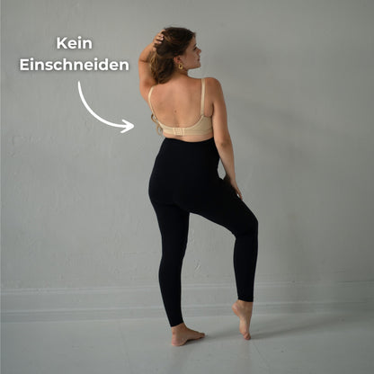 Das Bild zeigt eine werdende Mutter, die einen beige Umstandsmode-Still-BH trägt. Sie dreht sich seitlich und hebt eine Hand an ihren Nacken, um den BH zu präsentieren. Der Text „Kein Einschneiden“ ist neben ihr positioniert, um hervorzuheben, dass der BH dank seines Designs keine unangenehmen Druckstellen hinterlässt. Der Hintergrund ist schlicht, sodass der Fokus auf der Mutter und dem Umstandsmode-Still-BH liegt.